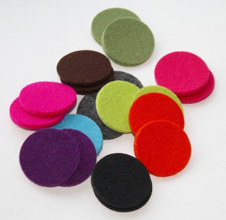 May include: Assortment of felt circles in various colors, including pink, green, purple, red, black, brown, and blue. The circles are arranged in a random pattern on a white surface.