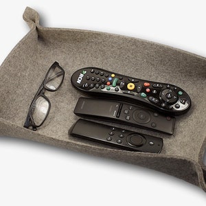 May include: A gray felt tray with three remote controls and a pair of glasses. The remotes are black and have buttons and a directional pad. The glasses are black and have a clear lens.