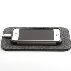 May include: A gray felt charging pad with a white smartphone on top. A white charging cable is plugged into the phone.