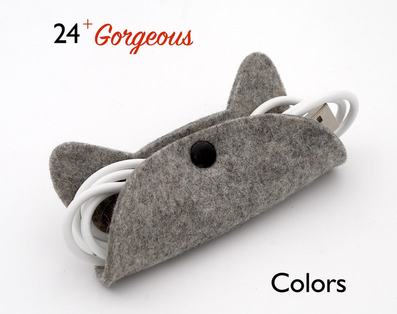 May include: Grey felt cord organiser shaped like a cat with a button closure. The organiser is holding a white charging cable. The text "24+ Gorgeous" is in the top left corner of the image. The text "Colors" is in the bottom right corner of the image.
