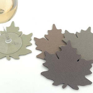 May include: Four felt maple leaf coasters in shades of brown, green, and gray. One coaster is under a wine glass.