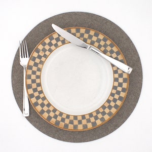 Puede incluir: Un plato blanco con un borde a cuadros marr&oacute;n y gris se encuentra sobre un mantel individual de fieltro gris. Un tenedor y un cuchillo de plata est&aacute;n colocados en el plato.