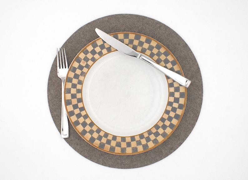 Puede incluir: Un plato blanco con un borde a cuadros marr&oacute;n y gris se encuentra sobre un mantel individual de fieltro gris. Un tenedor y un cuchillo de plata est&aacute;n colocados en el plato.