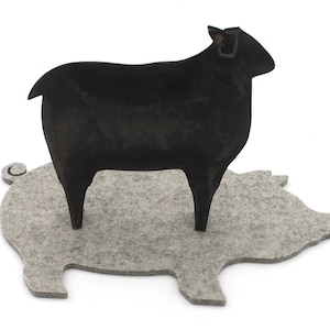 May include: A black metal sheep figurine standing on a gray felt pig-shaped coaster.