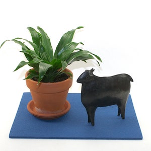 May include: A black ceramic sheep figurine on a blue felt mat, next to a potted green plant in a terracotta pot.