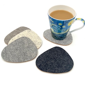 May include: A set of four felt coasters in pebble shapes with varying shades of gray, white, and charcoal. One coaster supports a ceramic mug featuring a blue and yellow swirling pattern reminiscent of a starry night sky painting.