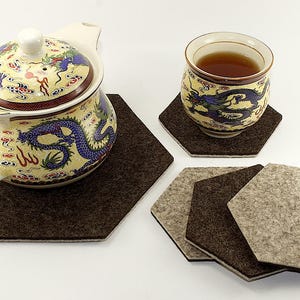 May include: A set of six hexagonal felt coasters in brown and beige. The coasters are designed to protect surfaces from heat and scratches. A teapot and teacup with a dragon design are sitting on the coasters.