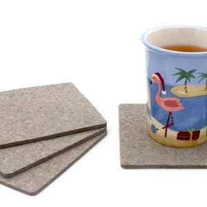 May include: Four gray felt coasters with a blue mug with a pink flamingo and palm trees on it. The mug is filled with a brown liquid.