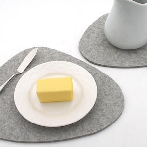 May include: Two grey felt coasters, one with a white ceramic jug and the other with a white plate and a stick of butter.