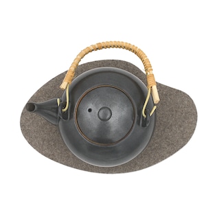May include: A black ceramic teapot with a woven bamboo handle sits on a gray felt coaster. The teapot has a round body and a lid with a small knob.