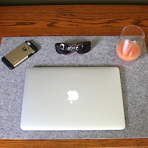 May include: A gray felt desk mat with a laptop computer, a cell phone in a case, sunglasses, and a glass of orange juice.