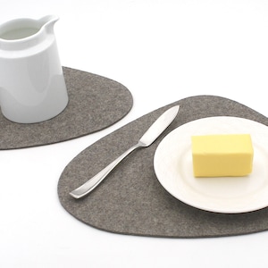 May include: Two gray felt placemats, one with a white pitcher and the other with a white plate, a butter knife, and a stick of butter.