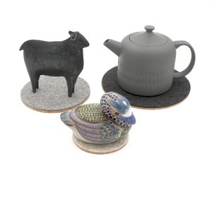 May include: Three felt coasters with different ceramic figurines on top. A black sheep, a gray teapot, and a colorful duck.