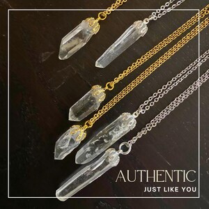 Peut inclure: Quatre colliers avec des pointes de cristal sur des chaînes dorées et argentées. Les pointes de cristal sont transparentes et ont un sertissage doré. Les colliers sont superposés sur une surface en bois foncé. Le texte "AUTHENTIC JUST LIKE YOU" est en bas de l'image.