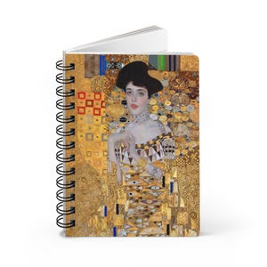 May include: Spiral-bound notebook featuring a portrait of a woman in a gold and patterned dress. The cover art is a reproduction of a famous painting. The notebook has a black spiral binding and white pages.