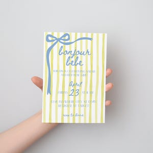 May include: A yellow and white striped baby shower invitation with a blue bow and the text "bonjour bebe". The invitation says "Join us in celebrating [name] and the arrival of the girl" and "April 23 at 11 am".