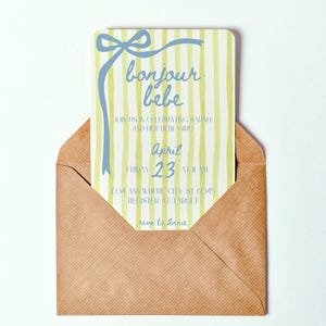May include: A yellow and white striped baby shower invitation with blue text that reads "bonjour bebe". The invitation includes the date "April 23" and the time "11 AM".