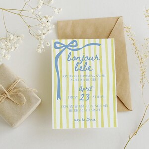 May include: A yellow and white striped baby shower invitation with a blue ribbon and bow. The text reads "bonjour bebe" and includes the date "April 23".