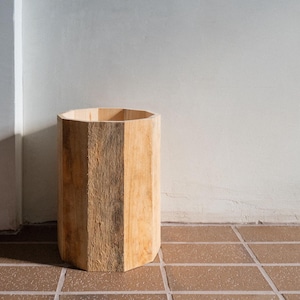 Puede incluir: Un macetero hexagonal de madera con un acabado de madera natural. El macetero está vacío y se encuentra sobre un suelo de baldosas.