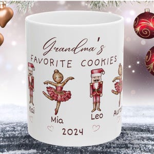 May include: White ceramic mug with a red and white illustration of a ballerina, a nutcracker, and the text "Grandma's Favorite Cookies" with the names Kai, Mia, Leo, and Aura and the year 2024.