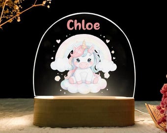 May include: A decorative night light featuring a cartoon unicorn with a rainbow and clouds. The name "Chloe" is printed above the unicorn. The light sits on a wooden base and has a glowing effect.