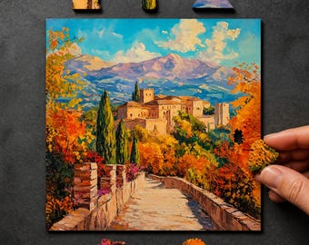 May include: A square jigsaw puzzle featuring an oil painting of a stone castle complex nestled in mountains, surrounded by autumn foliage and cypress trees, with a stone path leading toward the buildings. Several loose puzzle pieces are nearby.