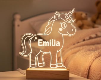 May include: A glowing unicorn night light with the name "Emilia" etched into the design. The light is made of clear acrylic and sits on a wooden base. The unicorn has a horn, mane, and tail.