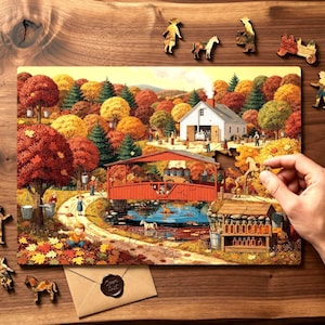 Könnte beinhalten: Ein farbenfrohes Holzpuzzle, das eine Herbstszene mit einer roten überdachten Brücke, einem weißen Bauernhaus und Herbstlaub darstellt. Mehrere Holzpuzzleteile sind um das Puzzle herum verstreut, darunter Figuren, Pferde und ein Wagen.