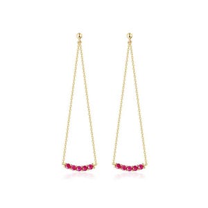 Puede incluir: Un par de pendientes colgantes dorados. Cada pendiente presenta una delicada cadena que suspende una fila curva de cinco pequeñas gemas rojas vibrantes. Los pendientes tienen un diseño simple y elegante.