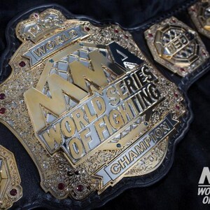 Pu&ograve; includere: Una cintura da campionato MMA World Series of Fighting in oro e argento. La cintura presenta le parole "MMA World Series of Fighting Champion" e il logo MMA. La cintura &egrave; su uno sfondo nero.