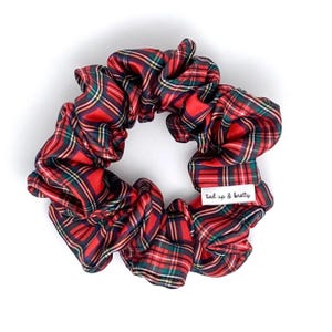 May include: A red, green, and navy tartan scrunchie made from a silky fabric. The scrunchie features a label that says "tied up & knotty". This hair accessory is a festive and stylish addition to any hairstyle.