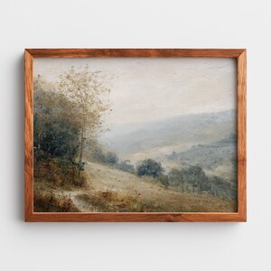 Puede incluir: Pintura de paisaje enmarcada con una paleta de colores apagados. La obra representa una ladera con árboles y un camino, bajo un cielo brumoso. El marco es de madera.