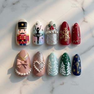 May include: A collection of ten artificial nails with various designs. The designs include a nutcracker, a ballerina, glitter, snowflakes, bows, pearls, Christmas trees, and a key. The nails are painted in a variety of colors, including red, white, pink, and blue.