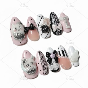 May include: A set of ten artificial nails with various designs. The nails feature a range of colors, including pink, white, and black, and are adorned with bows, lace, and cartoon characters. Some nails have polka dots and floral accents.