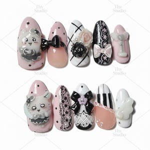 May include: A collection of ten almond-shaped artificial nails. Designs include a cartoon character, bows, lace, and floral accents. Colors include pink, white, black, and peach. Some nails feature polka dots and stripes. The nails are decorated with 3D elements.