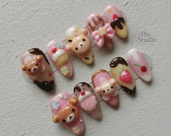 May include: A set of ten almond-shaped artificial nails with a variety of dessert-themed designs. Each nail features a different design, including teddy bears, bows, cupcakes, and strawberries, in shades of pink, brown, and white.