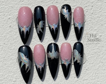 May include: A set of ten artificial nails with a pointed oval shape. The nails alternate between black and pink glitter. Each nail features a silver bat design and a silver glitter accent at the base.