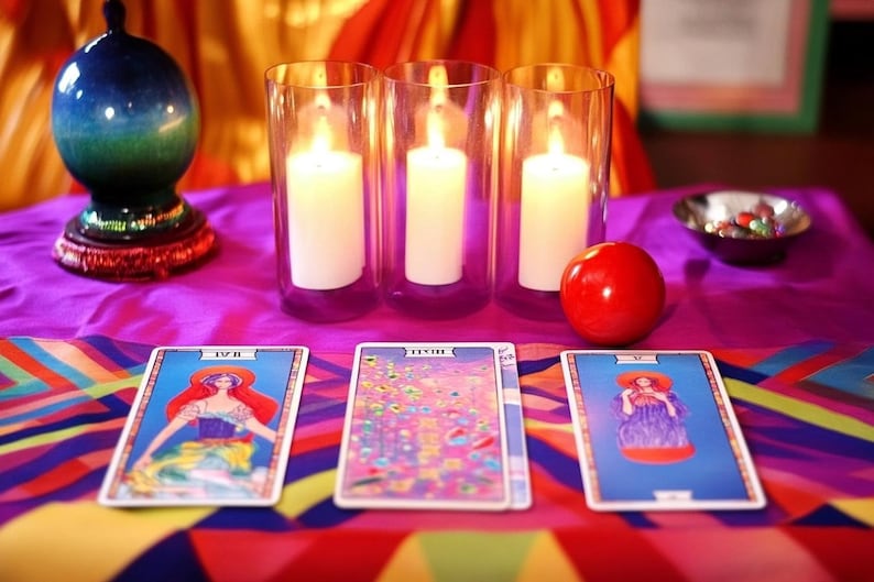 Pu&ograve; includere: Tre candele accese in portacandele di vetro, una mela rossa, una sfera di cristallo su un supporto e tre carte dei tarocchi su una tovaglia da tavolo colorata. Le carte sono etichettate con "IV", "XVII" e "XI".