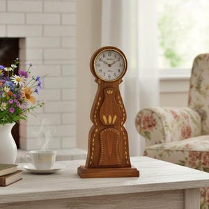 May include: A wooden clock with a round face and gold detailing sits on a table. A vase of flowers, books, and a teacup are also on the table. A floral armchair and a fireplace are in the background.