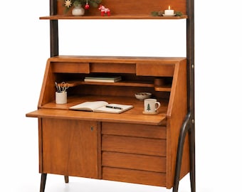 Op de afbeelding: Een houten secretaire in mid-century stijl met een neerklapbaar werkblad, een onderkast met sleutelgat en vier horizontale lades. Het meubelstuk is voorzien van een bovenplank, donkerbruine verticale steunen en een open werkruimte.