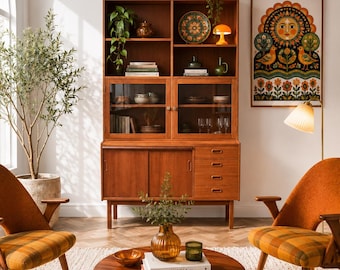 Könnte beinhalten: Ein Holzschrank mit verglasten Schränken und Schubladen, flankiert von zwei orangefarbenen karierten Sesseln und einem runden Couchtisch aus Holz. Ein gerahmter Druck mit Sonnenmotiv hängt an der Wand und eine hohe Pflanze steht links.