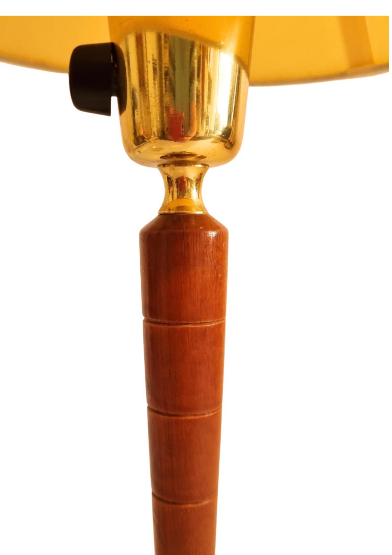 May include: A close-up of a vintage lamp. The lamp features a wooden base with a series of stacked cylindrical sections. The lamp's upper portion has a gold-colored metal fixture and a yellow lampshade. A black switch is visible.