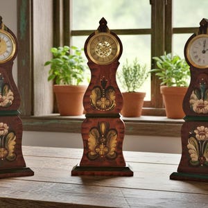 May include: Three decorative wooden clocks with floral patterns. Each clock features a round, gold-coloured clock face with black Roman numerals and hands. The clocks are brown with green and gold accents.