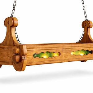 Op de afbeelding: Een hangende houten lamp met een natuurlijke afwerking. De lamp wordt opgehangen door zwarte kettingen en heeft decoratieve uitsparingen met groene en gele accenten. Het ontwerp is sierlijk en vintage-geïnspireerd.