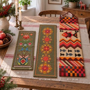 May include: Three rectangular wall hangings featuring cross-stitch embroidery. The left piece is olive green with floral and bird motifs, measuring 50 x 23 cm. The center piece is olive green with floral patterns, 67 x 26 cm. The right piece is multicolored with fish and geometric patterns, 83 x 24 cm.