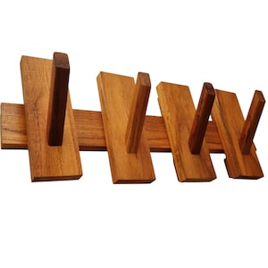 May include: A wall-mounted wooden coat rack featuring a horizontal base board with four vertical rectangular panels attached. Each panel has a single angled wooden peg extending outward, providing four distinct hooks for hanging items.