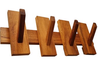 May include: A wall-mounted wooden coat rack featuring a horizontal base board with four vertical rectangular panels attached. Each panel has a single angled wooden peg extending outward, providing four distinct hooks for hanging items.