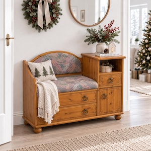 Op de afbeelding: Een houten halbank met een gestoffeerde zitting met een subtiel bloemenpatroon, twee onderste lades en een zijkast met een lade en plank. Inclusief een crèmekleurige plaid en een kussen met drie geborduurde dennenbomen.