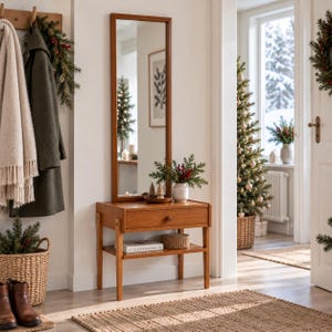 May include: A rectangular wooden wall mirror mounted above a wooden console table with a single drawer and a lower shelf. The console table features four straight legs and holds a small white vase with greenery, a book, and a woven basket.