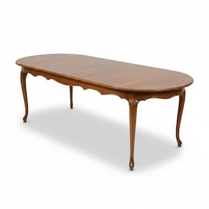 May include: A wooden oval dining table with a light brown finish. The table has a scalloped apron and four curved legs. The table is approximately 183 cm long and 102 cm wide.